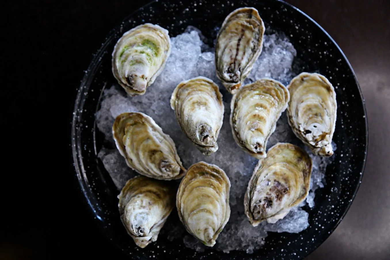A black bowl filled with ice and fresh oysters on top, viewed from above.