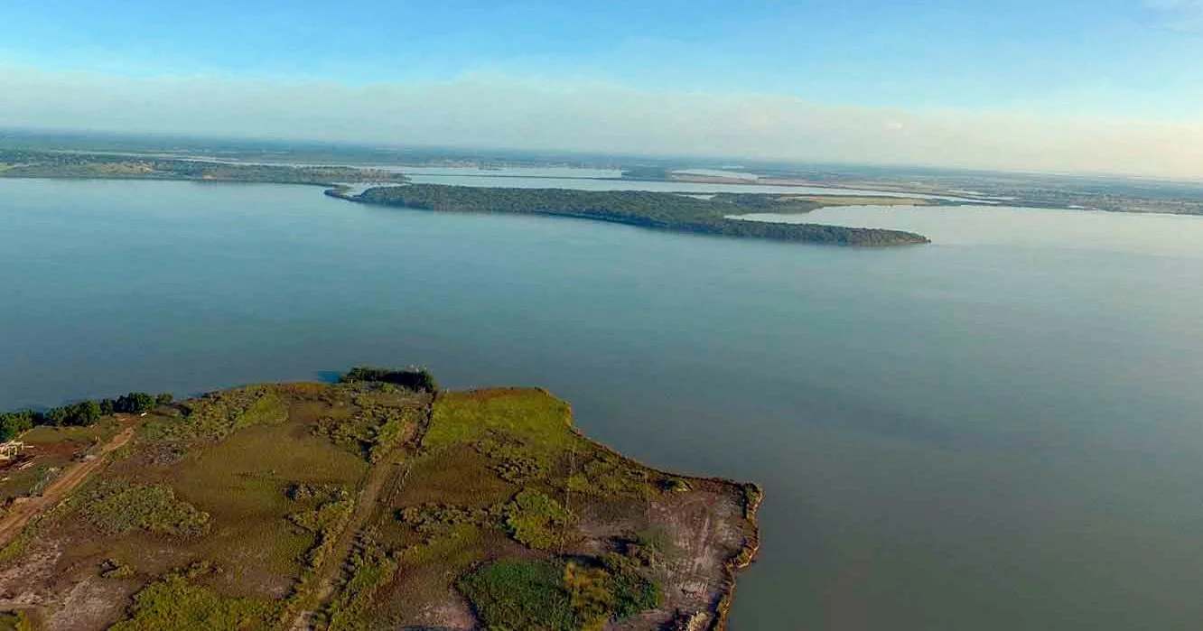 Aerial view of a large body of water with an island covered in trees and grassy areas in the foreground, and more land with trees and water in the background.