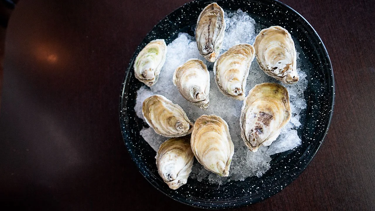 A black plate filled with ice and dozen oysters on ice