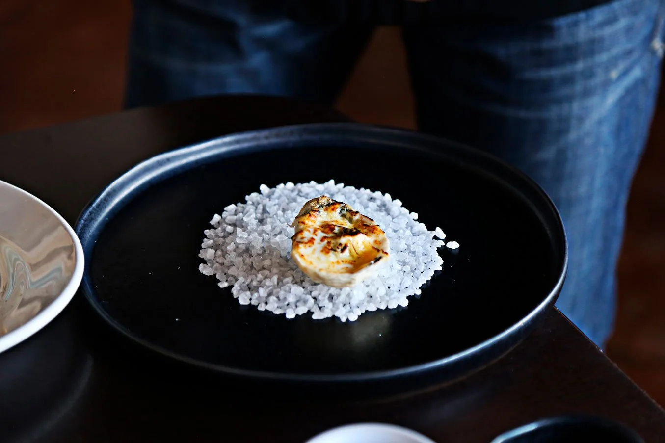 A black plate containing a pile of sea salt with a serving of grilled cheese on top.