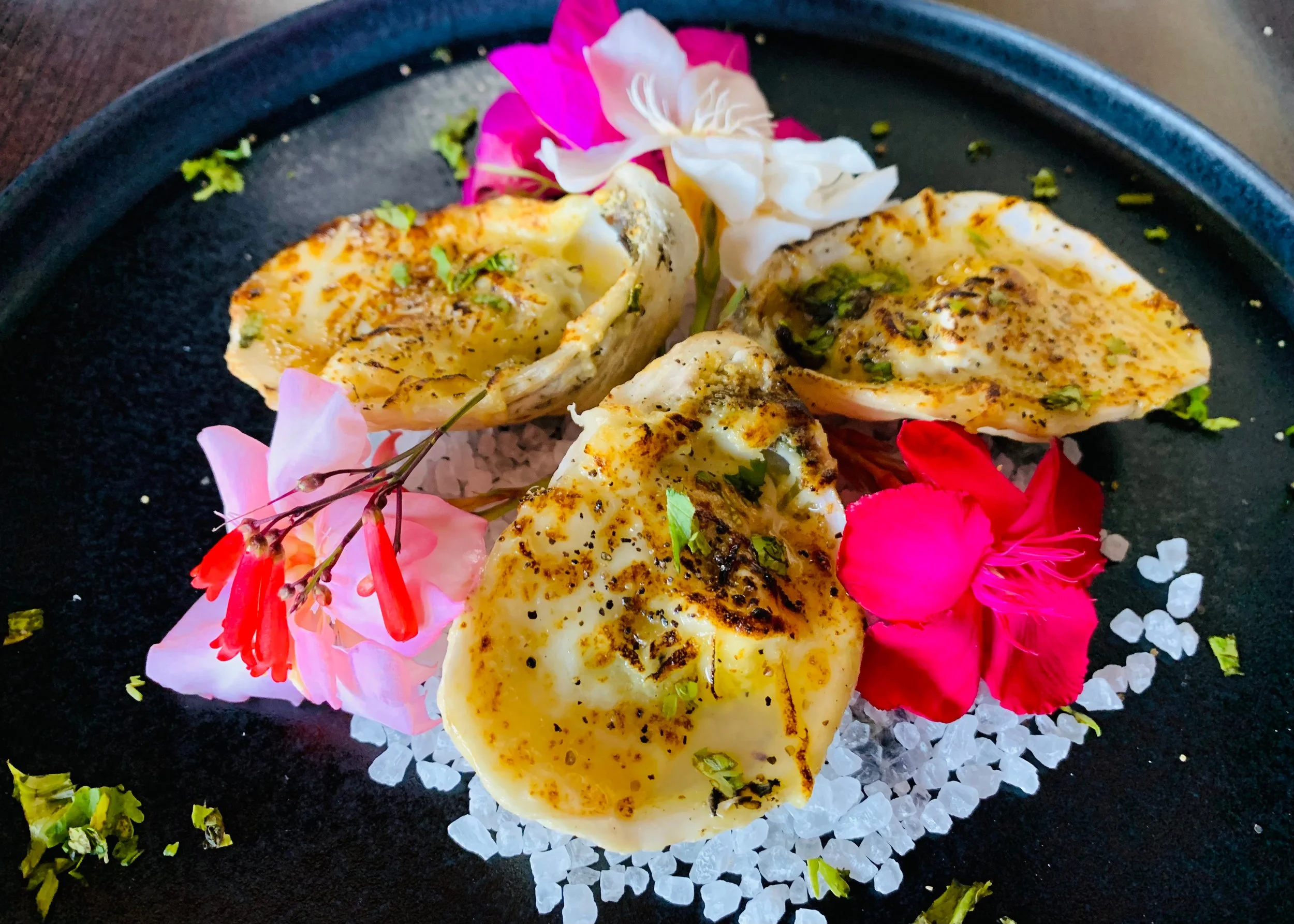 Grilled fish fillets garnished with herbs, served on a bed of crushed ice, and decorated with colorful edible flowers and petals.