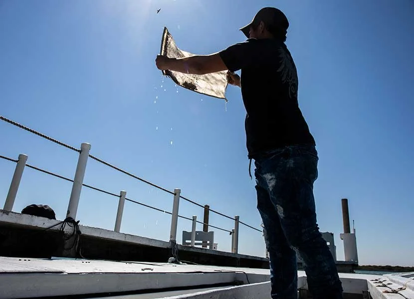 Person pouring water from a container on a boat with a blue sky background.