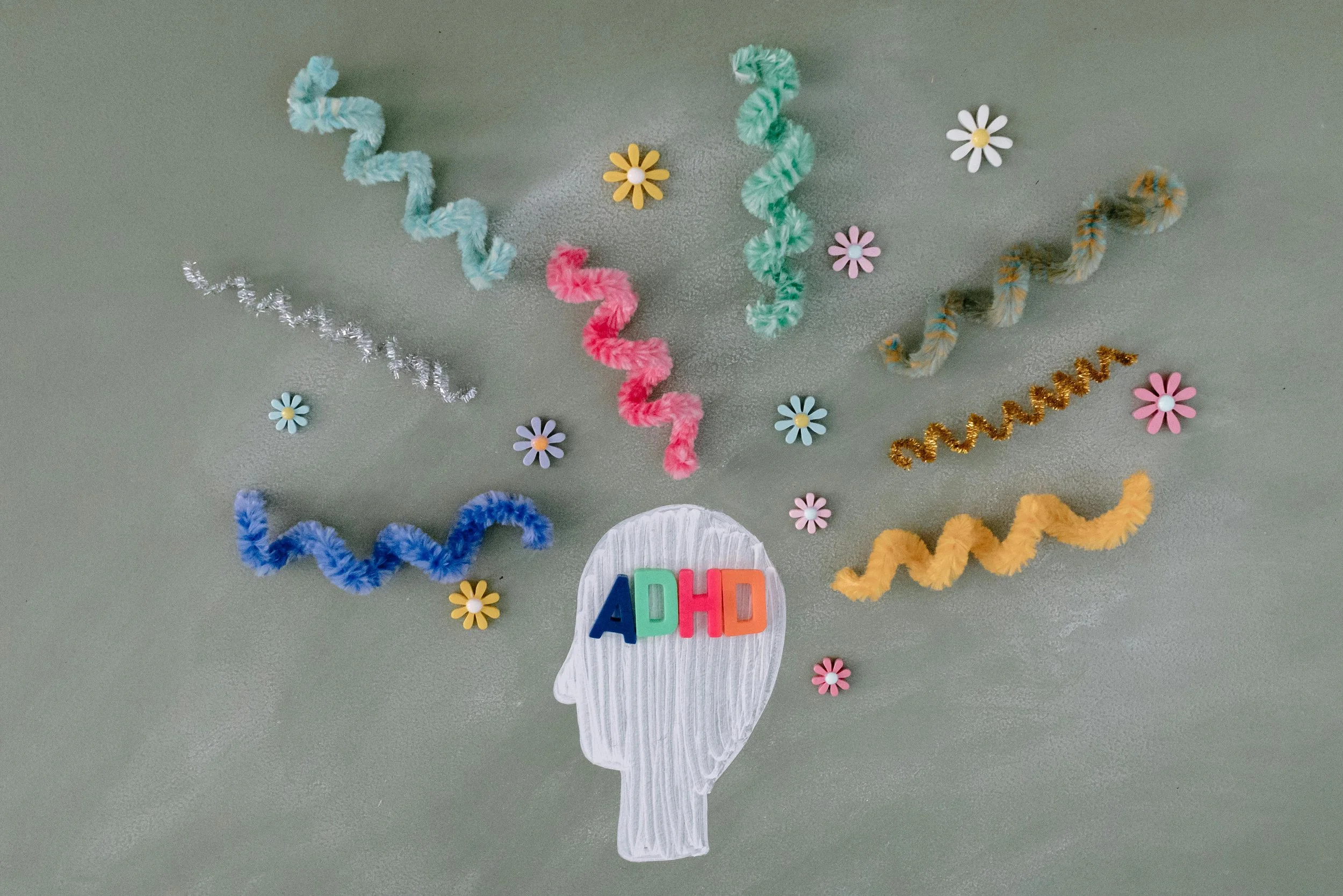 Colorful craft decorations on a table, including paper flowers, pipe cleaners twisted into spirals, and the word 'ADHD' on a paper cutout of a head.