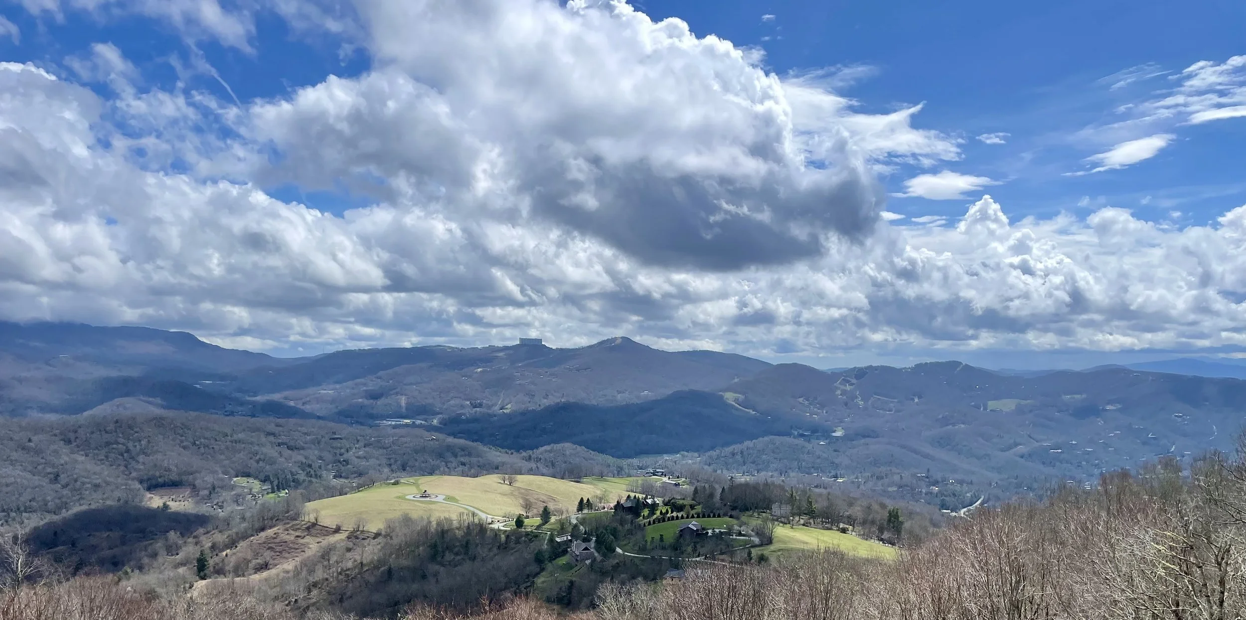 Scenic view of rolling hills and mountains under a partly cloudy sky.
