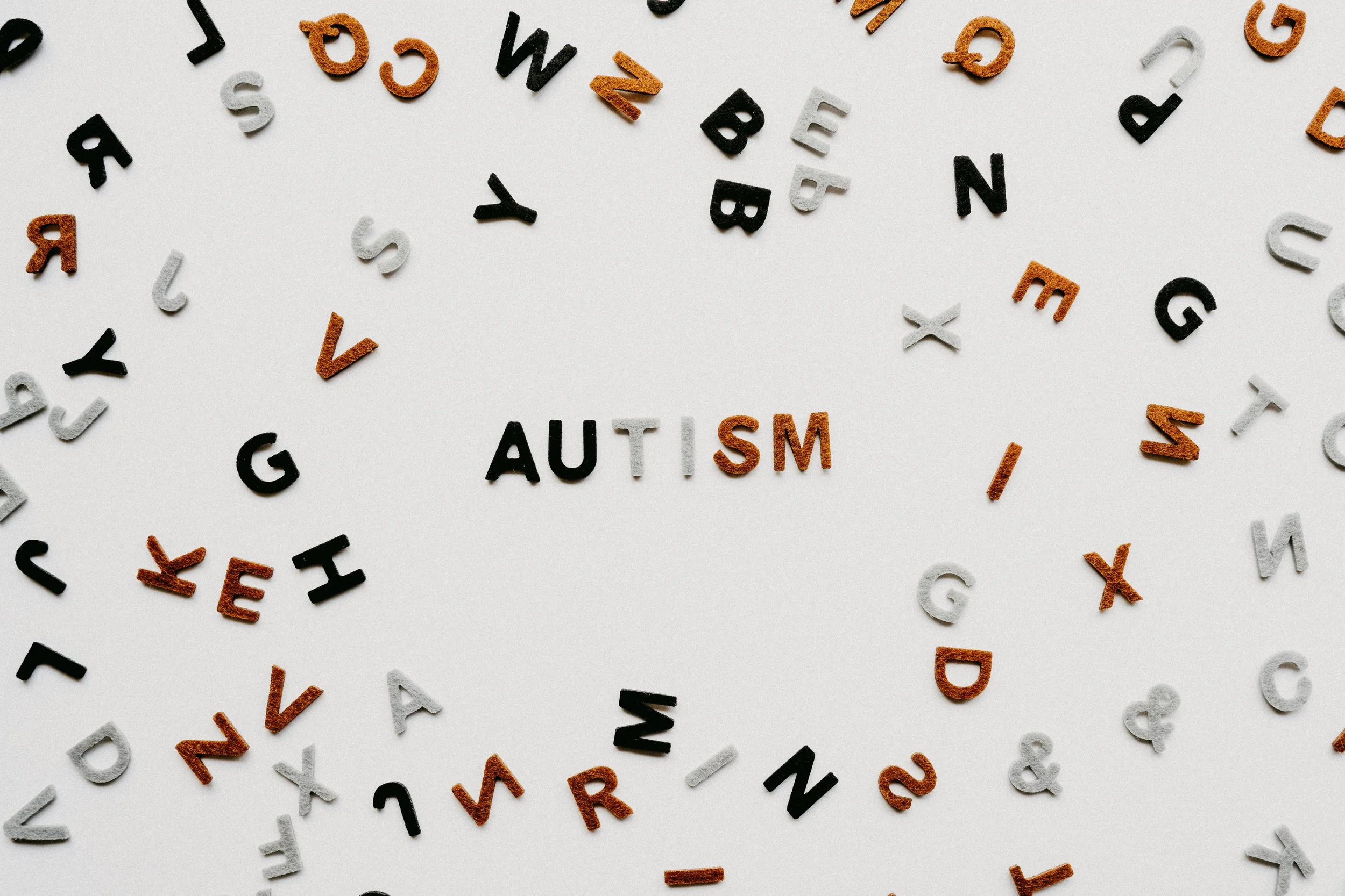 Scattered black, white, and orange letter tiles on a white background spelling out 'AUTISM' in the center.
