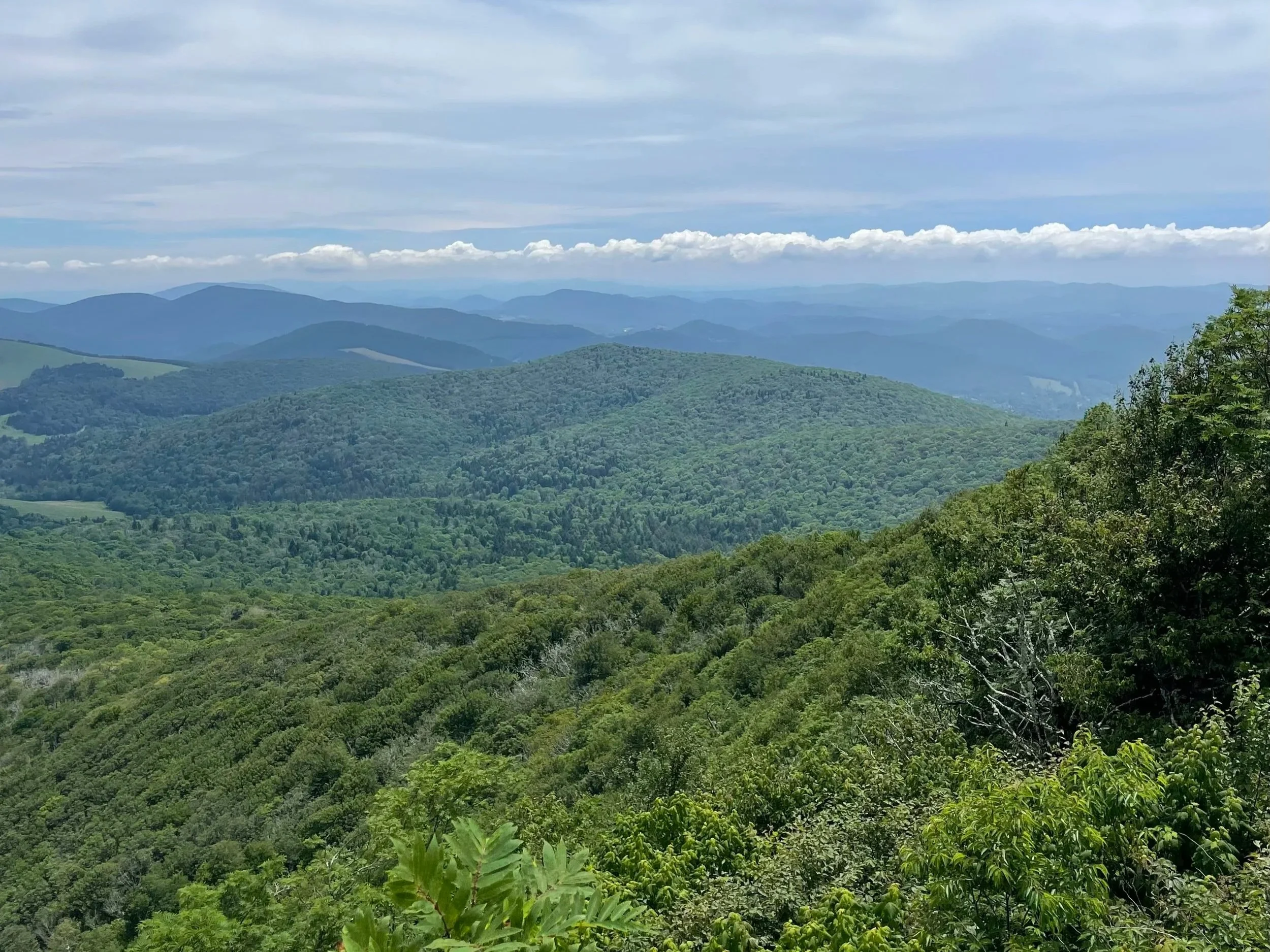 Landscape view of green, forested mountains with a partly cloudy sky above.