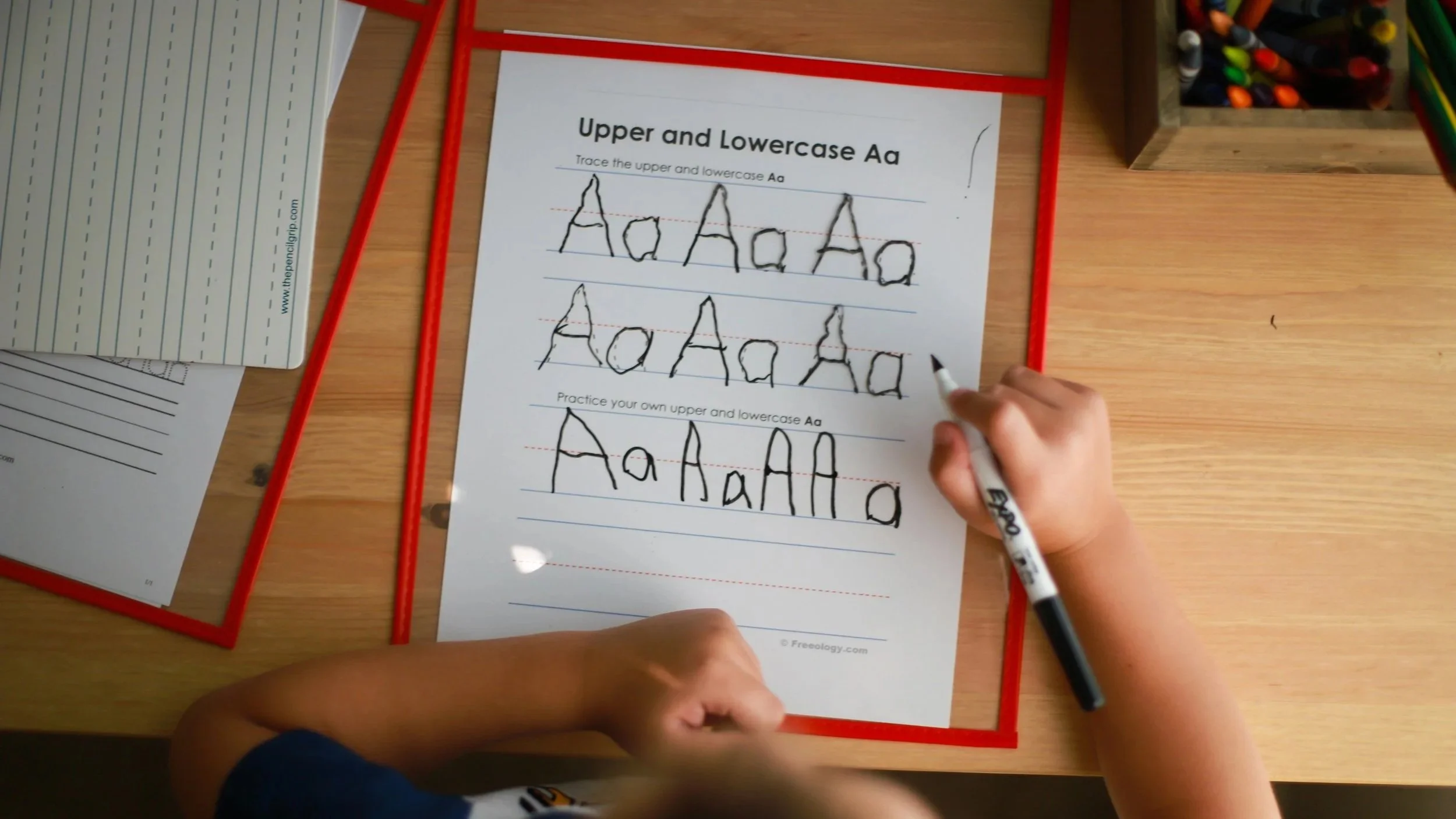 Child practicing tracing uppercase and lowercase letter A on a worksheet with a black marker.