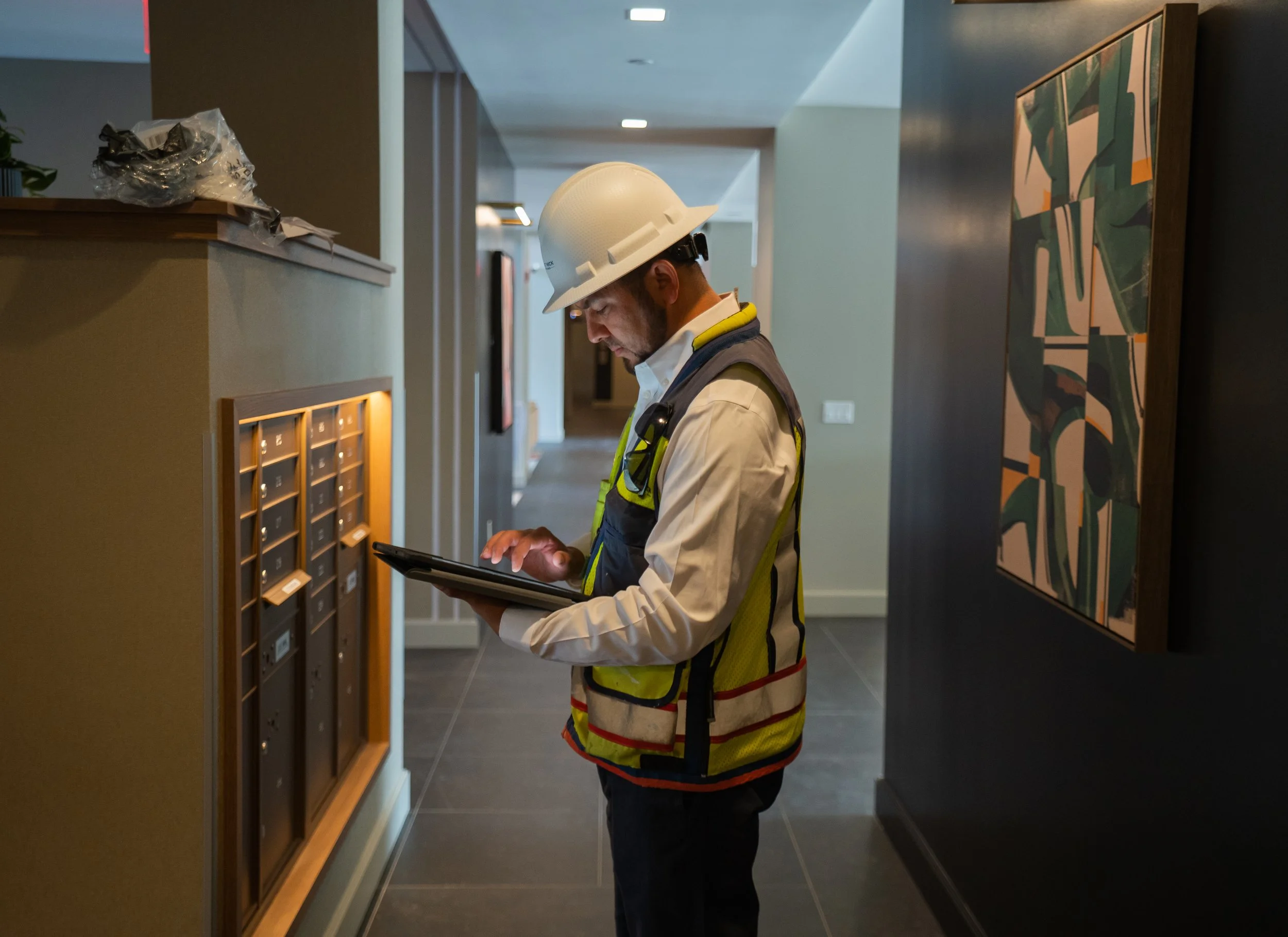 A construction worker wearing a white hard hat and reflective vest using a tablet in a modern indoor setting.