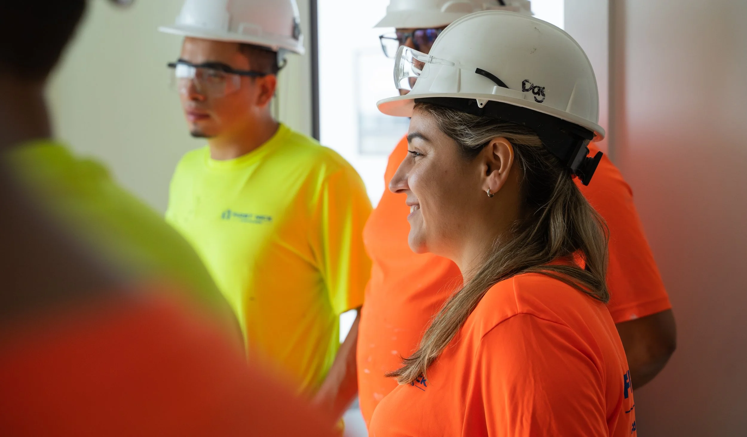 A group of construction workers wearing hard hats and safety glasses, engaging in a discussion inside a building.