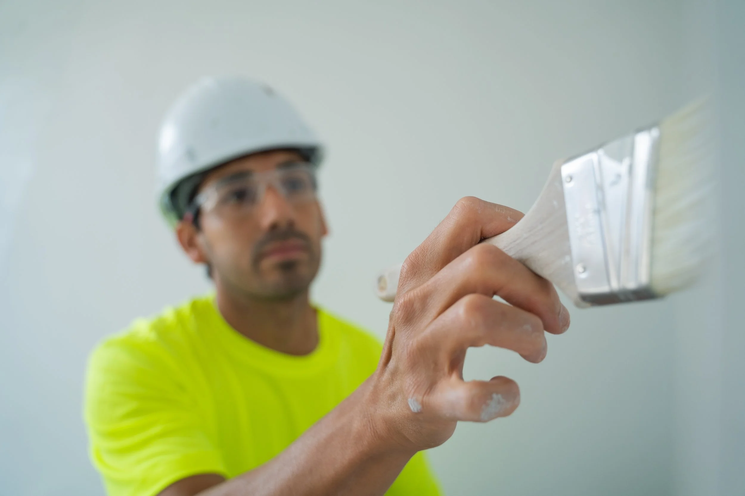 Close-up of a construction worker wearing safety gear and painting a wall with a paintbrush.