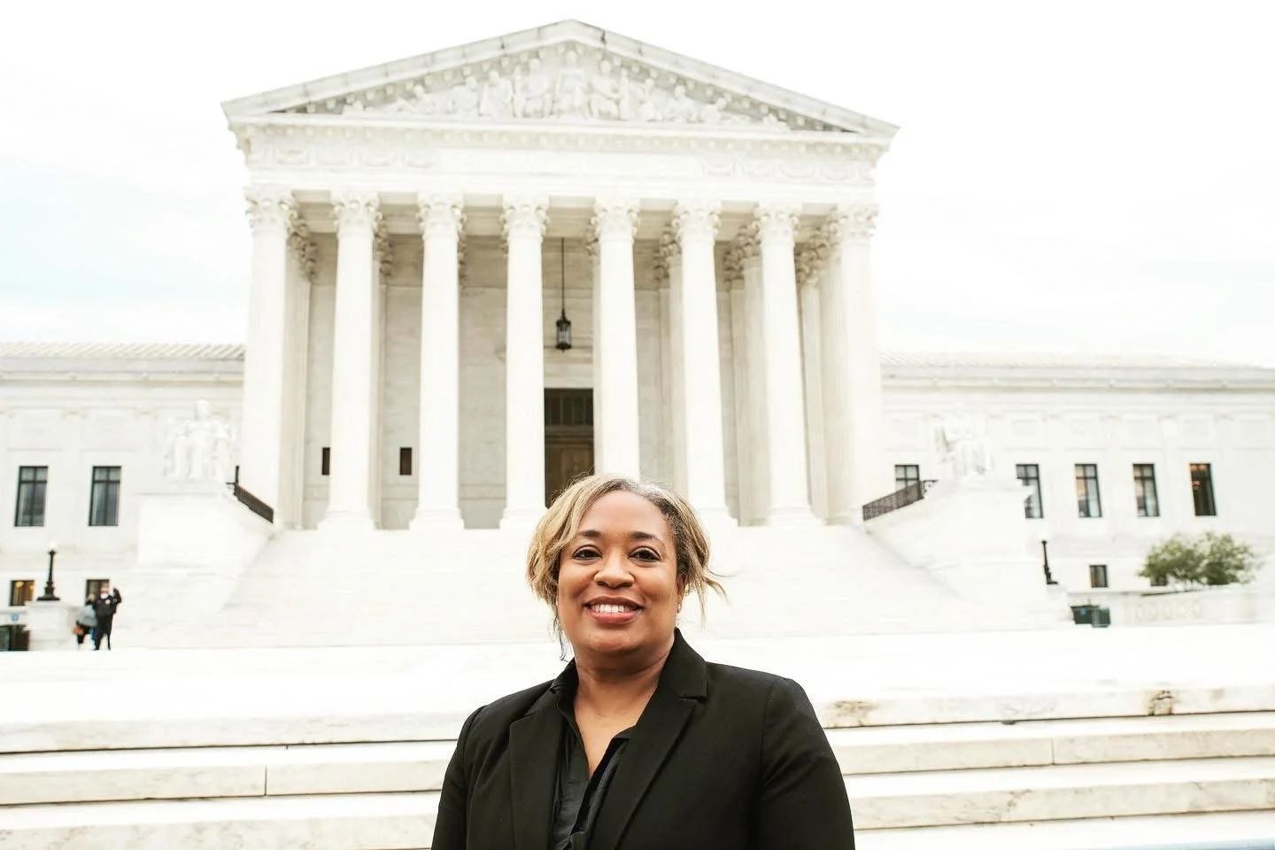 A woman smiling in front of the United States Supreme Court building with white marble steps and columns.