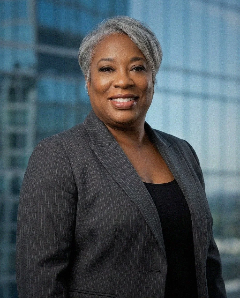 A woman with short gray hair wearing a dark gray pinstripe blazer and black top standing in front of a modern glass building.