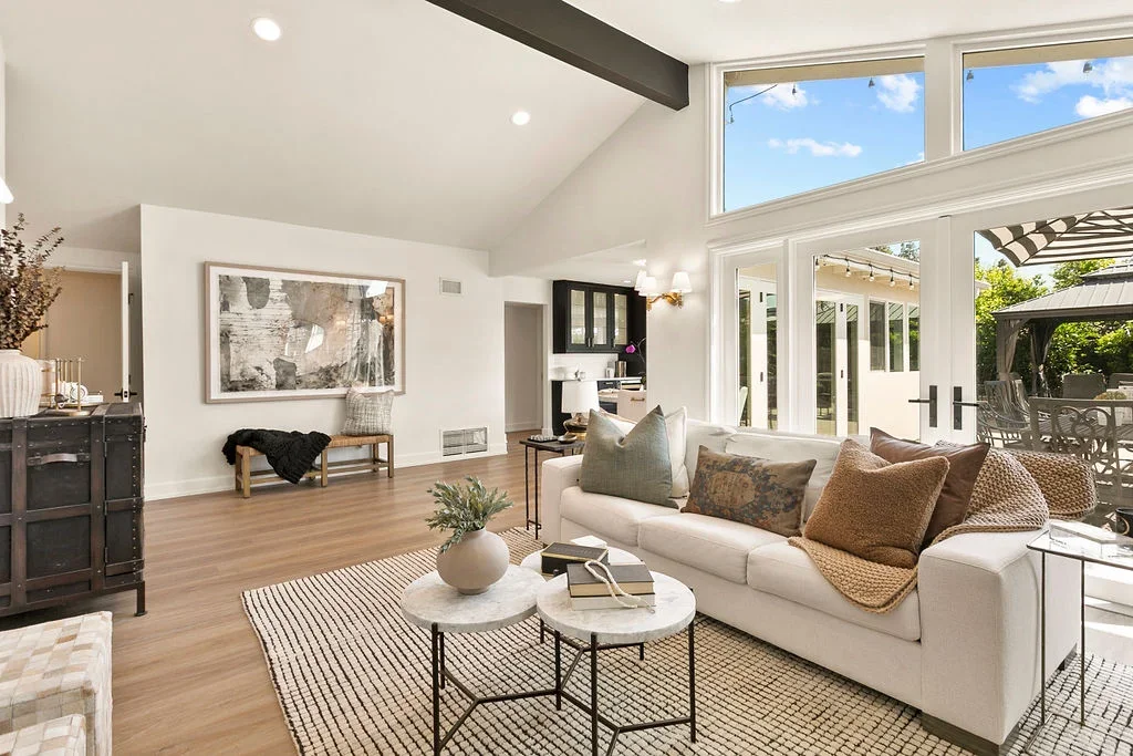 Bright, thoughtfully styled living room designed by NM Designs featuring layered neutral furnishings, vaulted ceilings, natural light, custom styling details, and indoor-outdoor living inspiration in Orange County, California.
