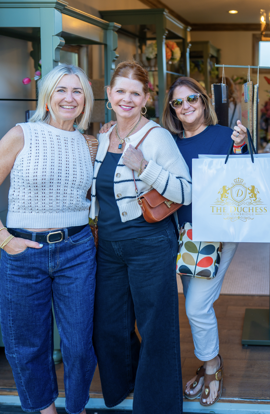 Three women smiling outside a shop with a sign that reads "The Duchess on Cambridge."