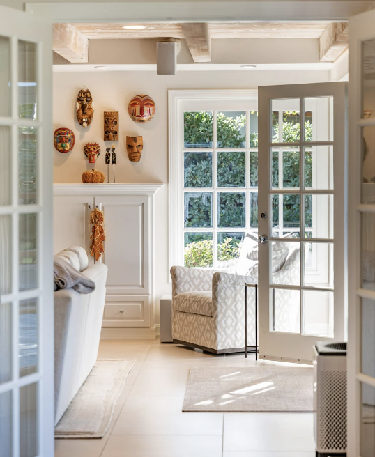 Bright living room with French door leading outside, decorated with colorful masks and artwork on the wall, with a cozy armchair near the window.