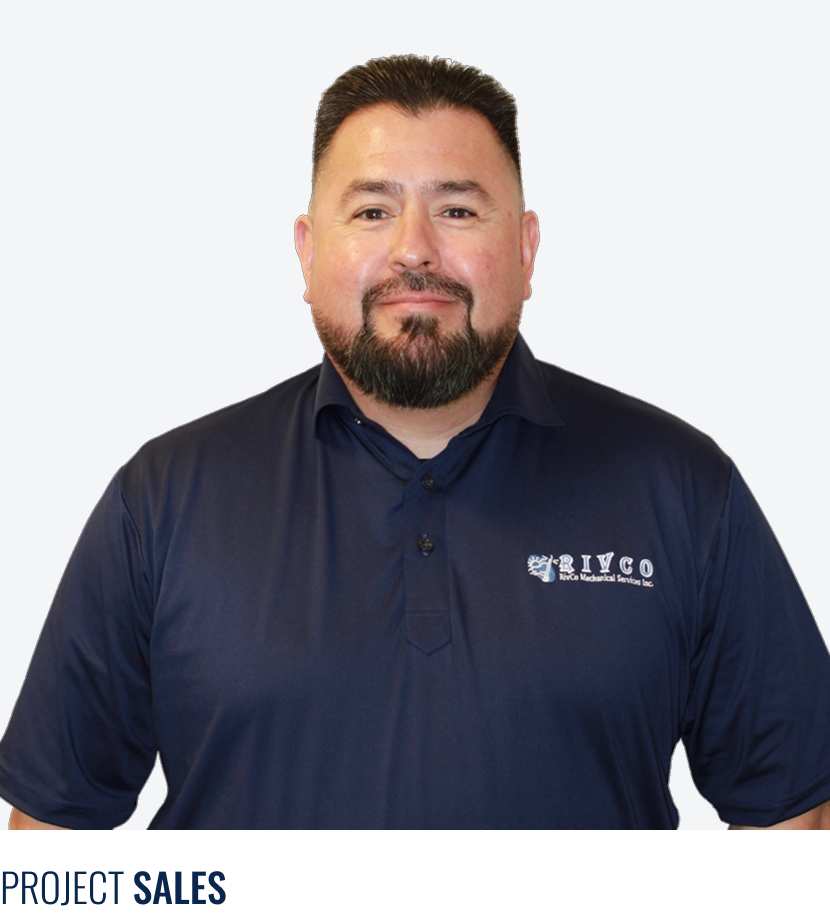 A man with short dark hair and a beard wears a navy blue polo shirt with a company logo on it, standing against a plain light background.