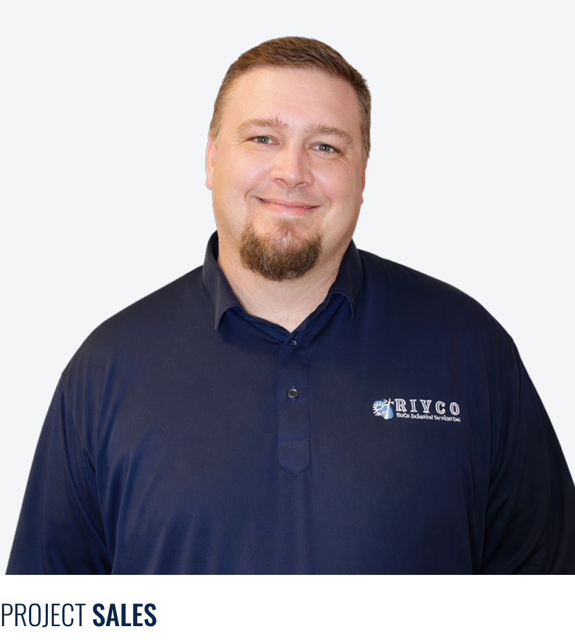 A man smiling wearing a dark navy blue collared shirt with the RIVCO logo on the chest, standing against a light gray background.