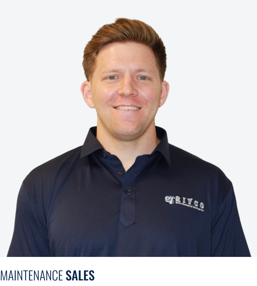 A smiling man with light skin and reddish-brown hair wearing a navy blue collared shirt with a company logo on it, standing against a plain light gray background.