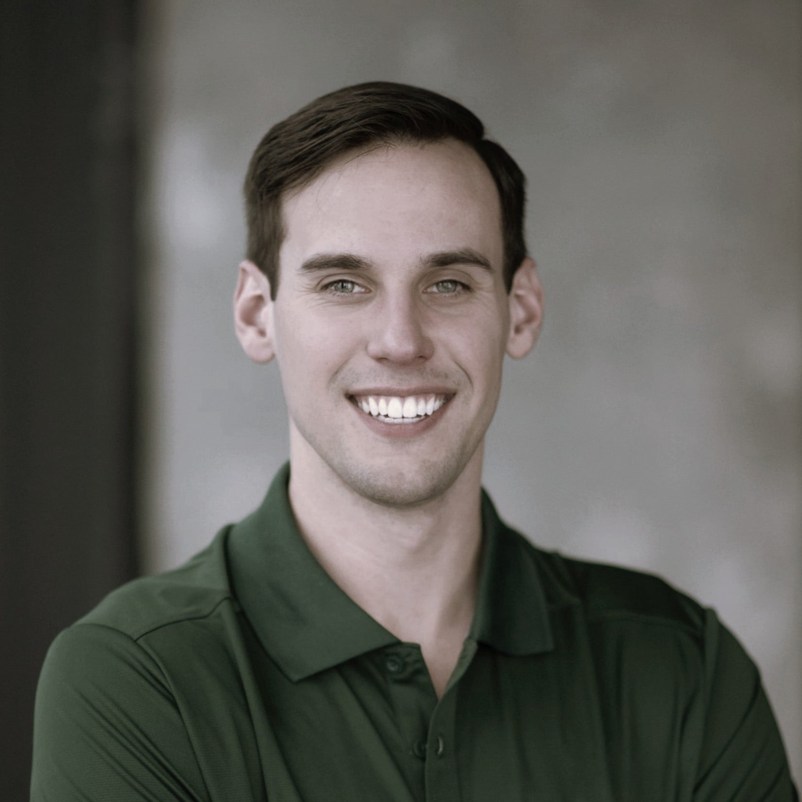Portrait of a smiling young man with short dark hair, wearing a dark green polo shirt, in an indoor setting.