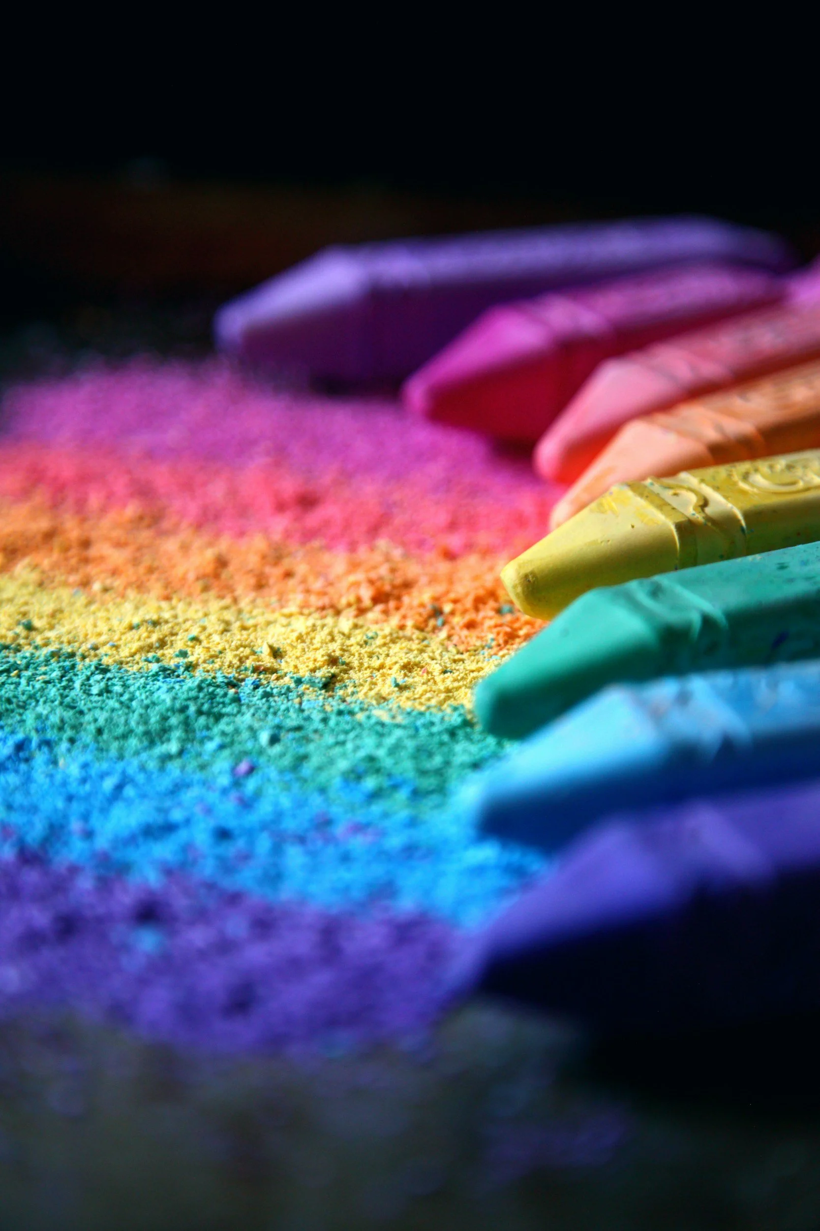 Colorful chalk sticks arranged with rainbow-colored chalk dust on a dark background