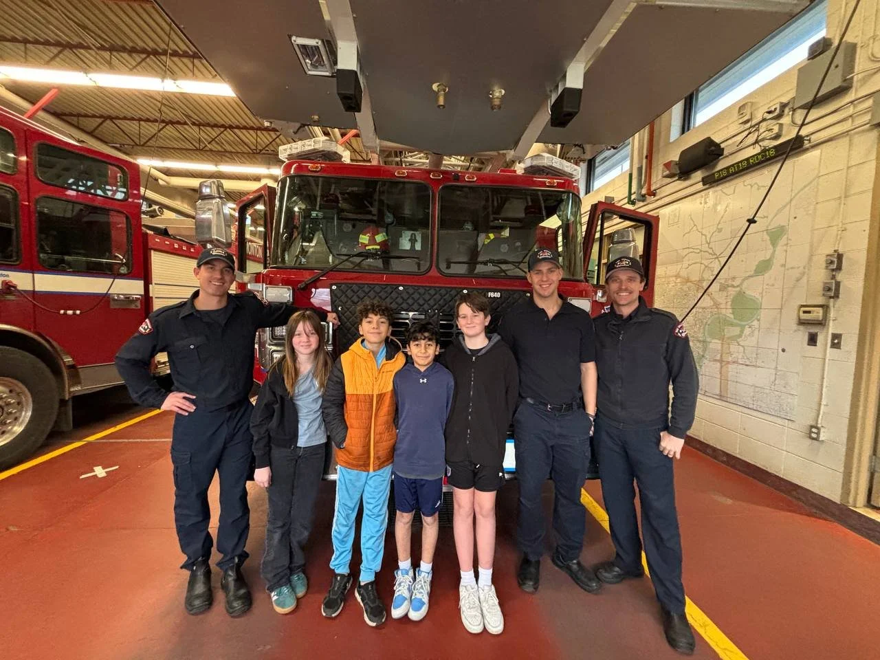 Children and firefighters posing in front of a fire truck inside a fire station.