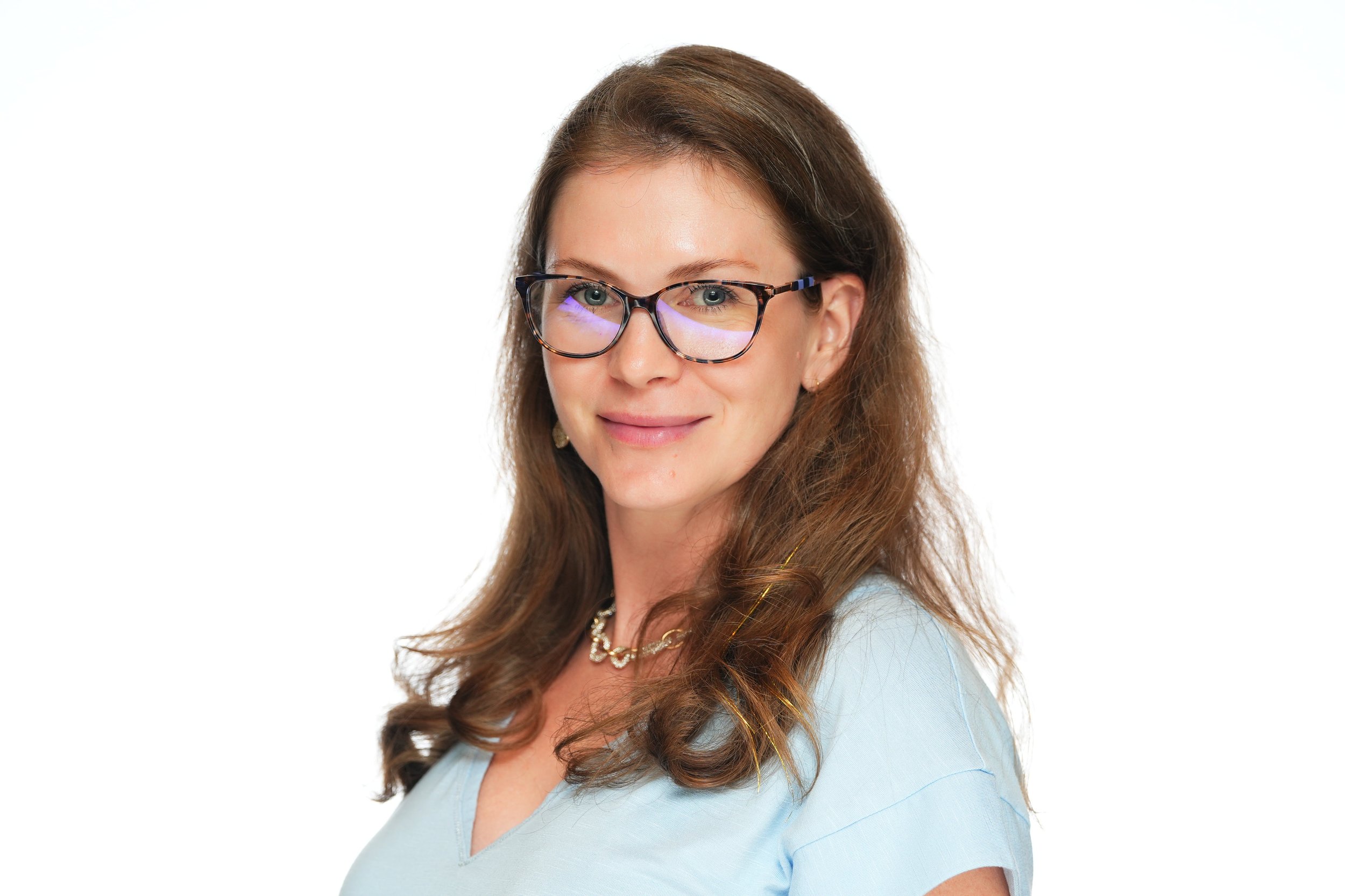 A woman with brown wavy hair and glasses smiling against a white background.