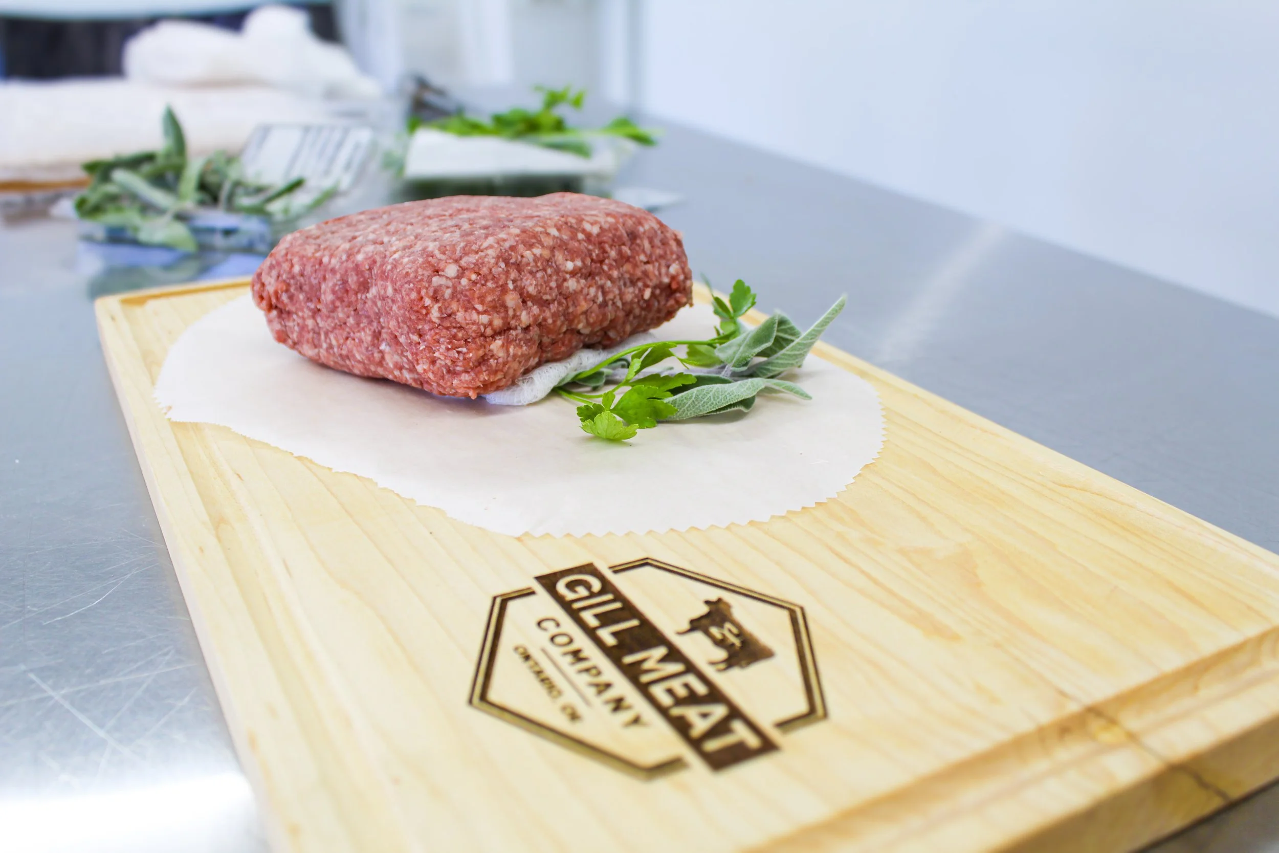 Raw juicy red local ground beef on a wooden cutting board with green herbs.