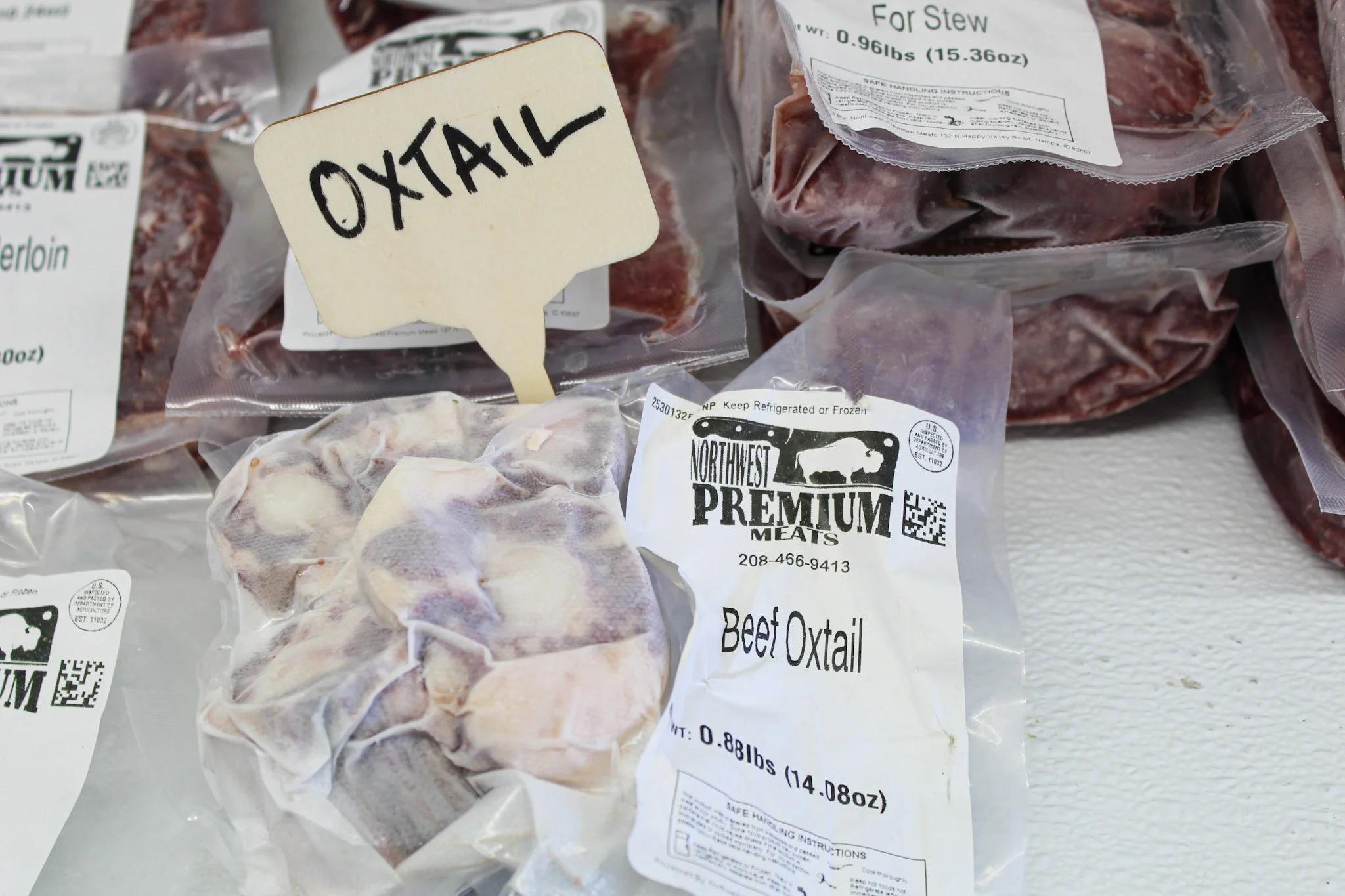 Packages of beef oxtail and other meat cuts on a white surface, with labels indicating the contents and weight.
