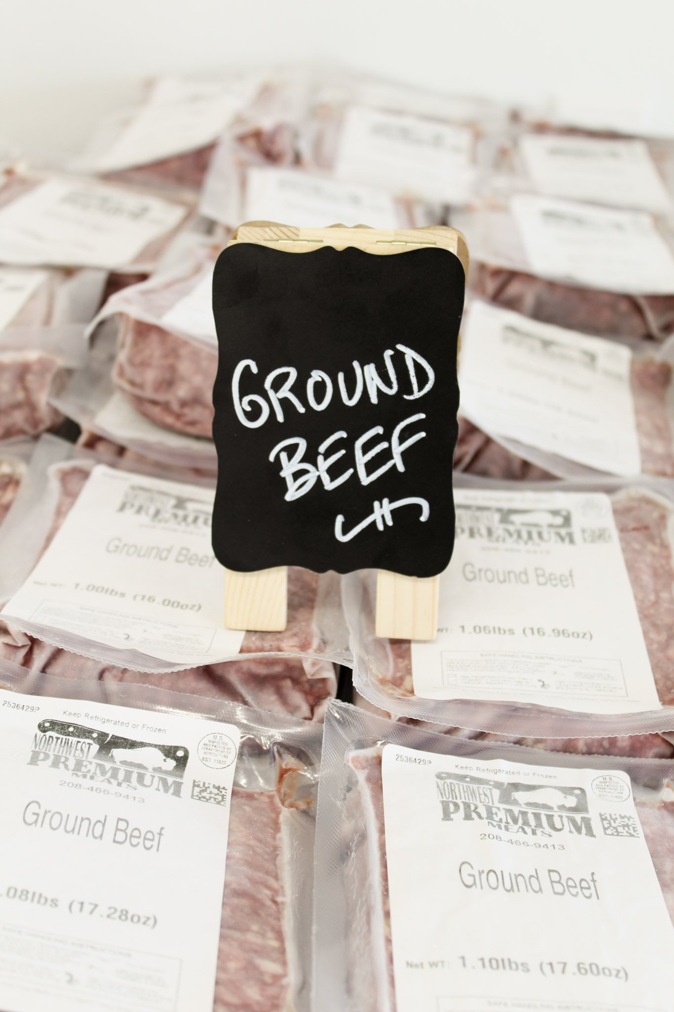 Packages of ground beef with a small blackboard sign that reads 'ground beef' in white letters.