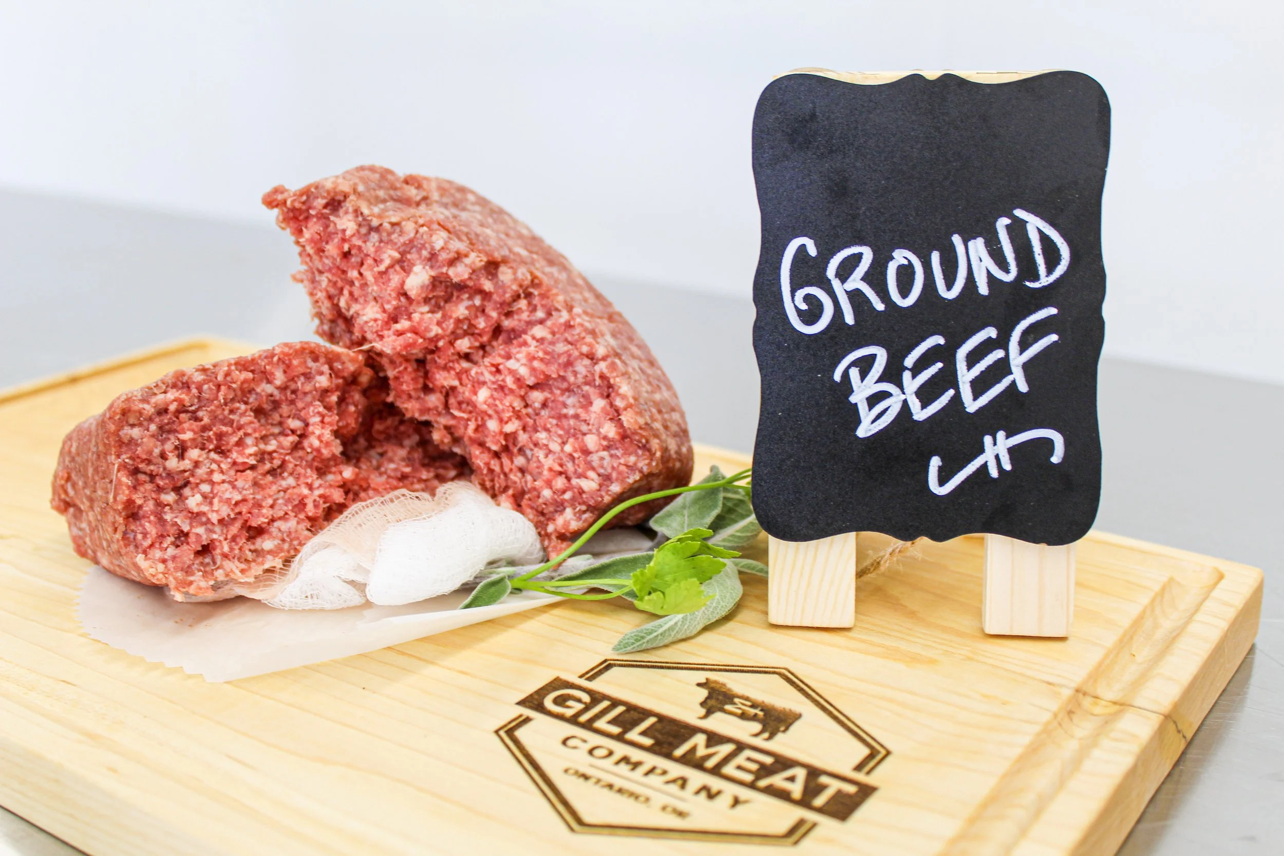 Raw local farm raised ground beef on a wooden cutting board with a handwritten sign that reads 'Ground Beef' in chalk.