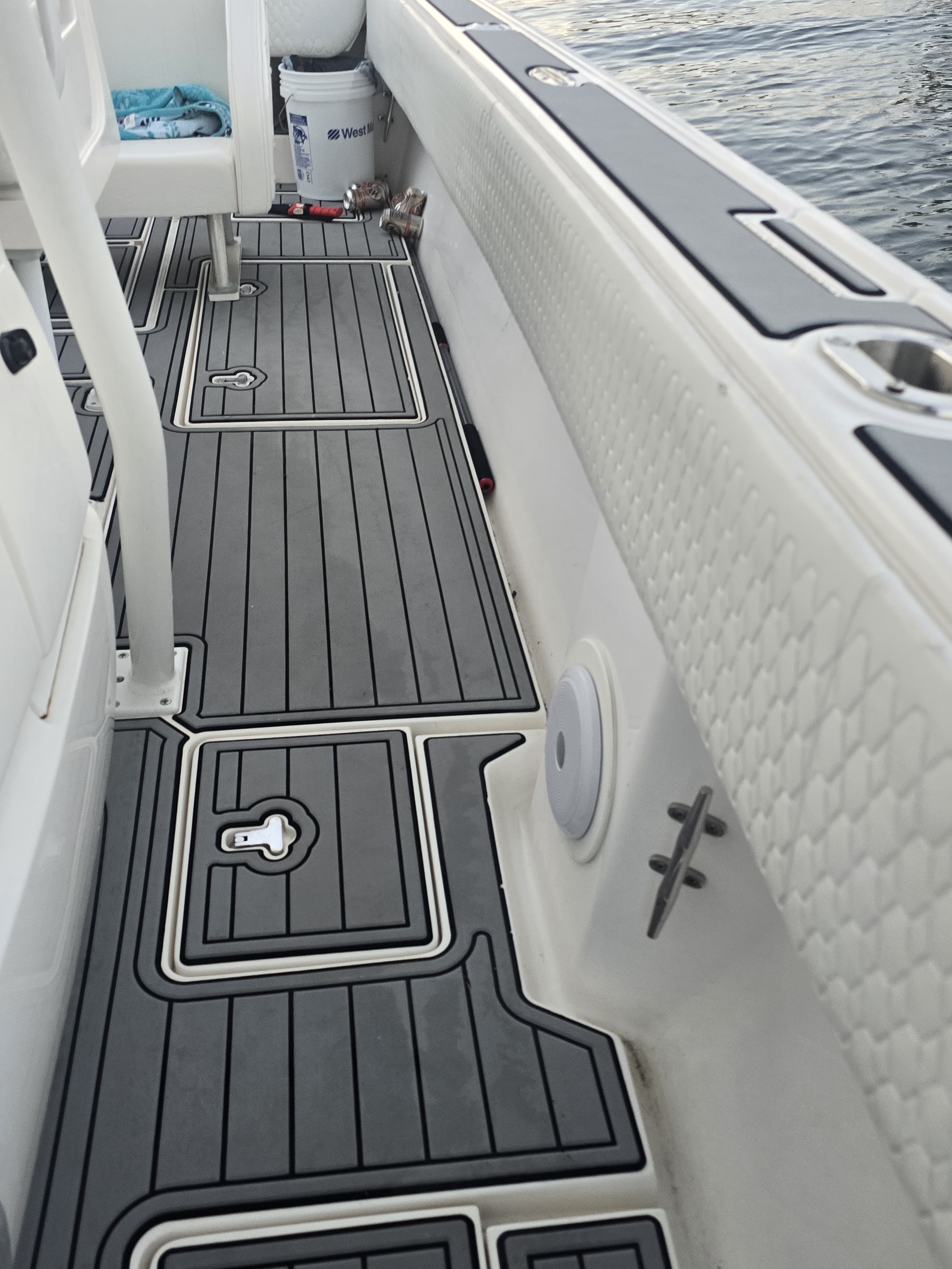 Close-up of the deck of a boat showing storage compartments, a speaker, and a section of the water nearby.