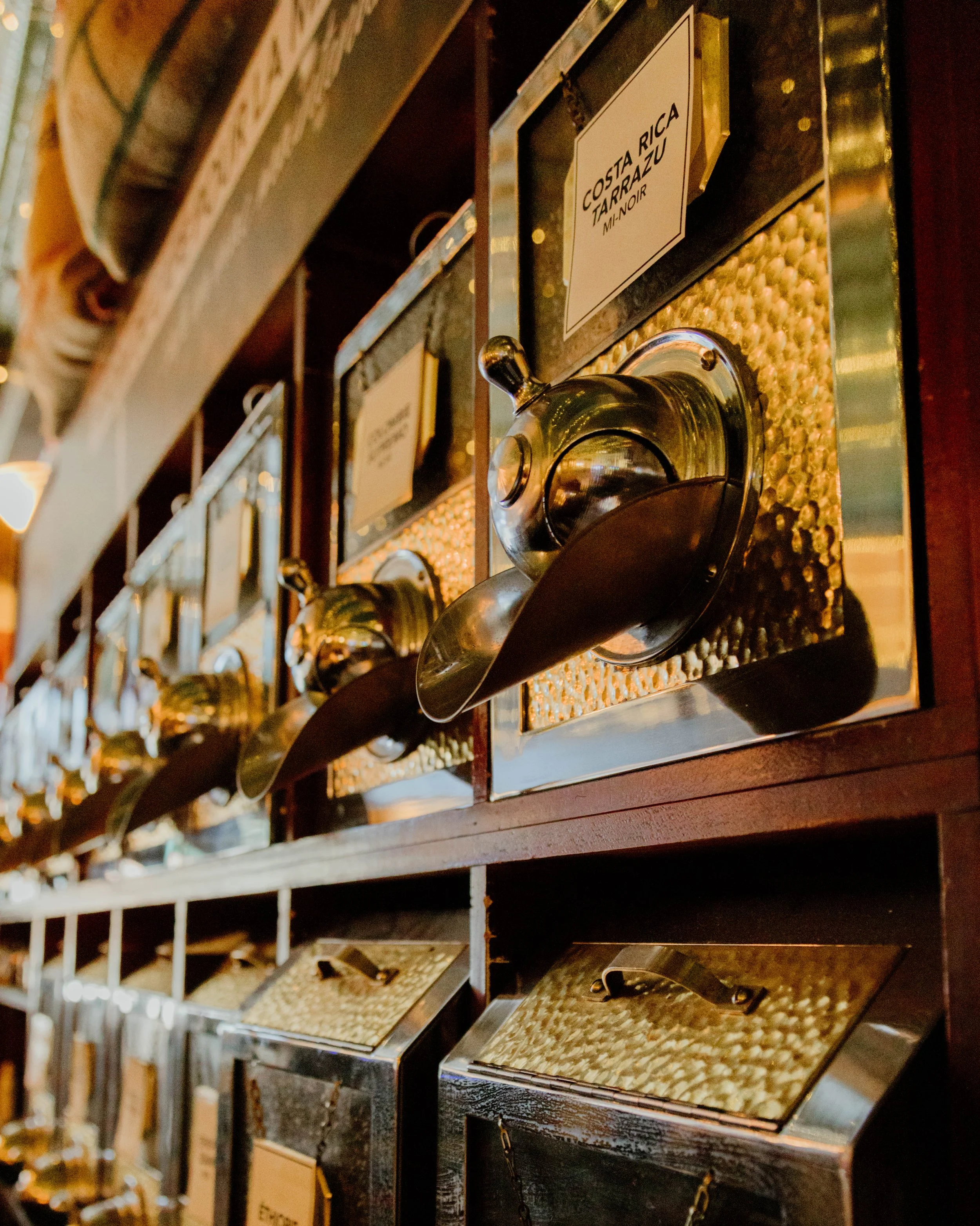 Étagère avec distributeur de Café en grains en vrac avec plusieurs origines et mélanges, la boîte en évidence est étiquetée Costa Rica Tarrazu.