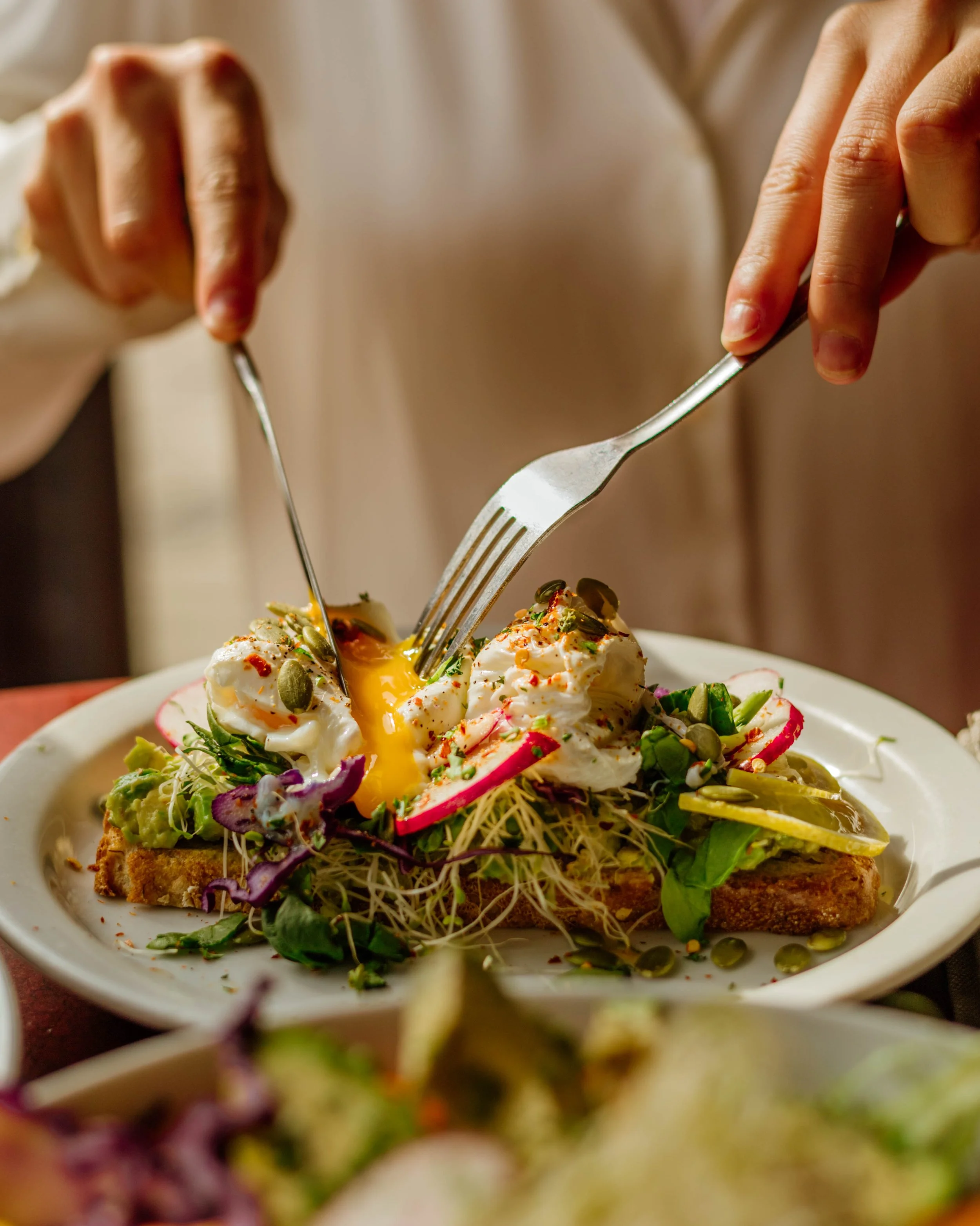 Une assiette avec une tartine au saumon fumé avec œufs pochés, légumes verts, radis, graines et sauce, décorée d'herbes et de graines.