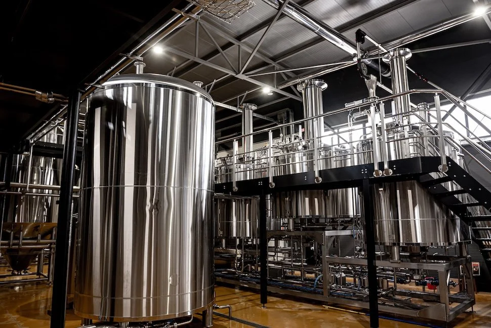 Industrial brewery equipment with large stainless steel tanks and piping inside a brewery.