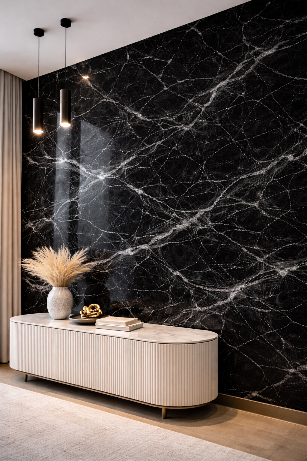A modern interior with a black marble accent wall, a white console table with a ribbed texture, a white vase with dried pampas grass, gold decorative objects, a stack of books, ceiling pendant lights, beige curtains, and a light-colored carpet.