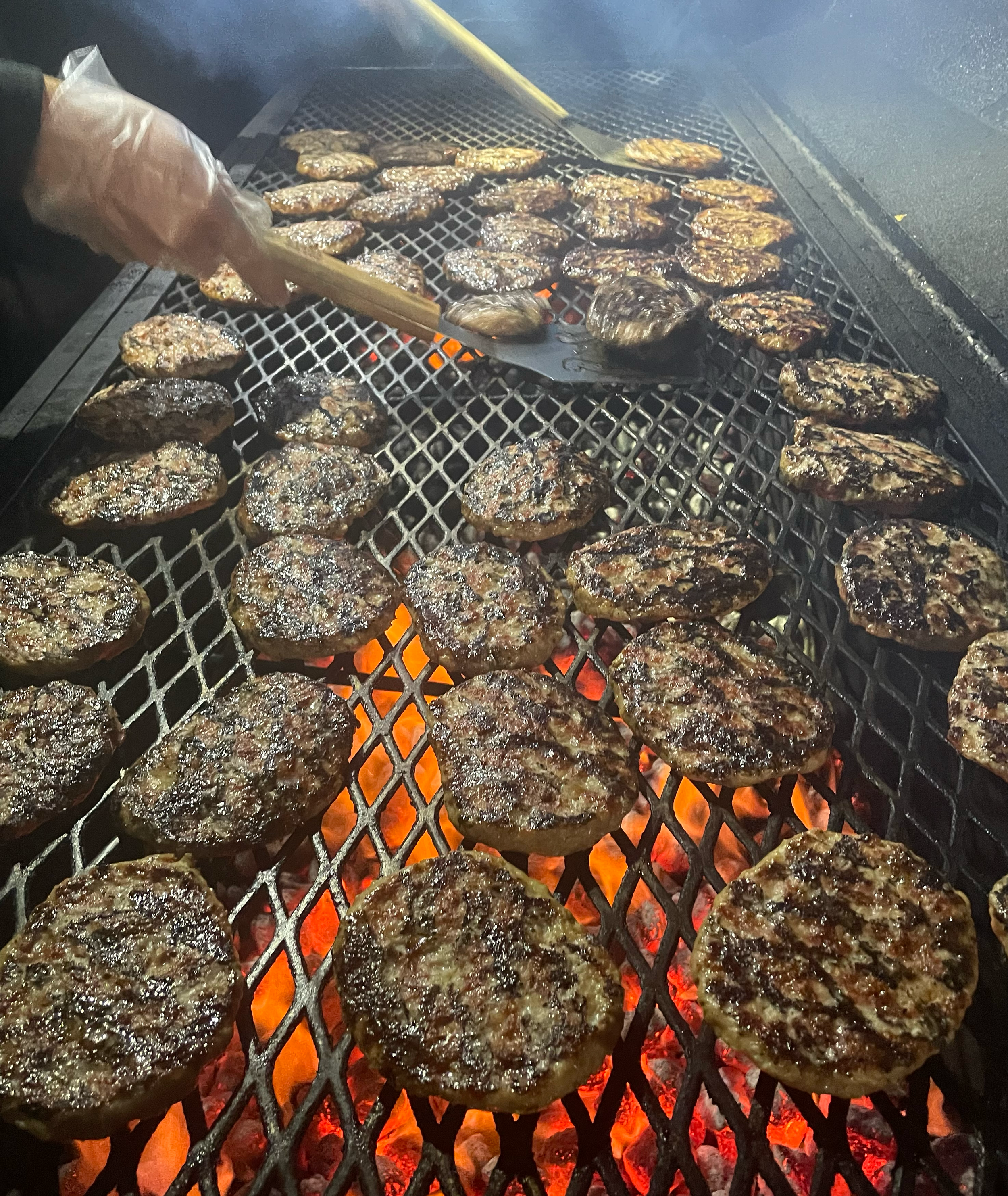 A Kings BBQ team member cooks beef patties  on a grill over open flames at a catering event in Northern, Indiana.