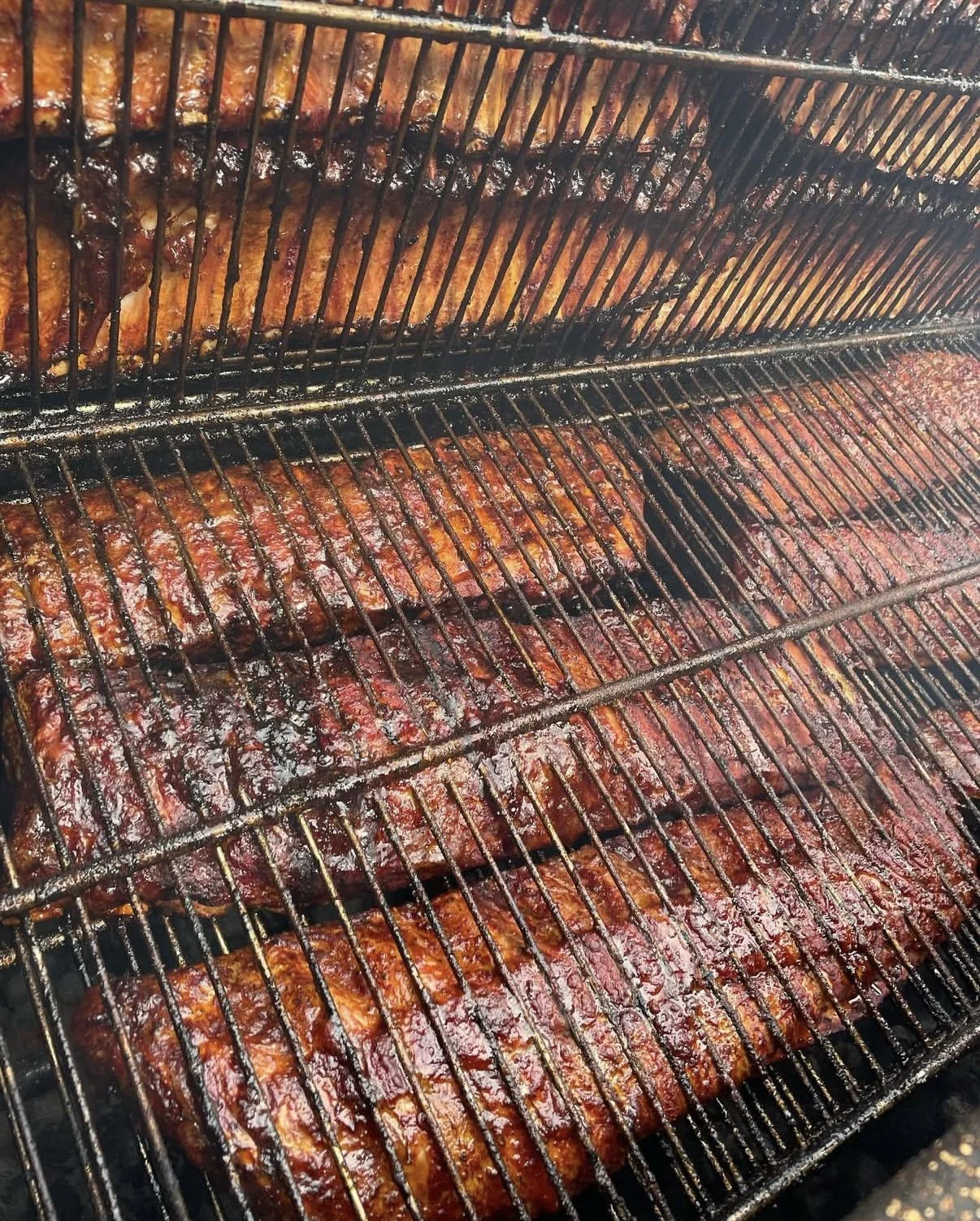 Racks of glazed, cooked ribs on a barbecue grill.