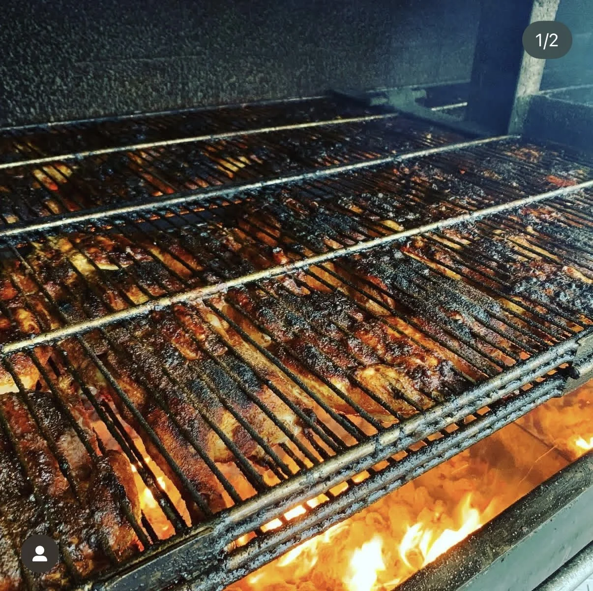 Barbecue grill with multiple racks of grilled meat cooking over an open flame.