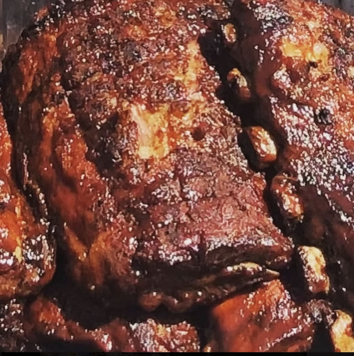 Close-up of cooked barbecue ribs coated in a thick, glossy sauce with visible char marks.