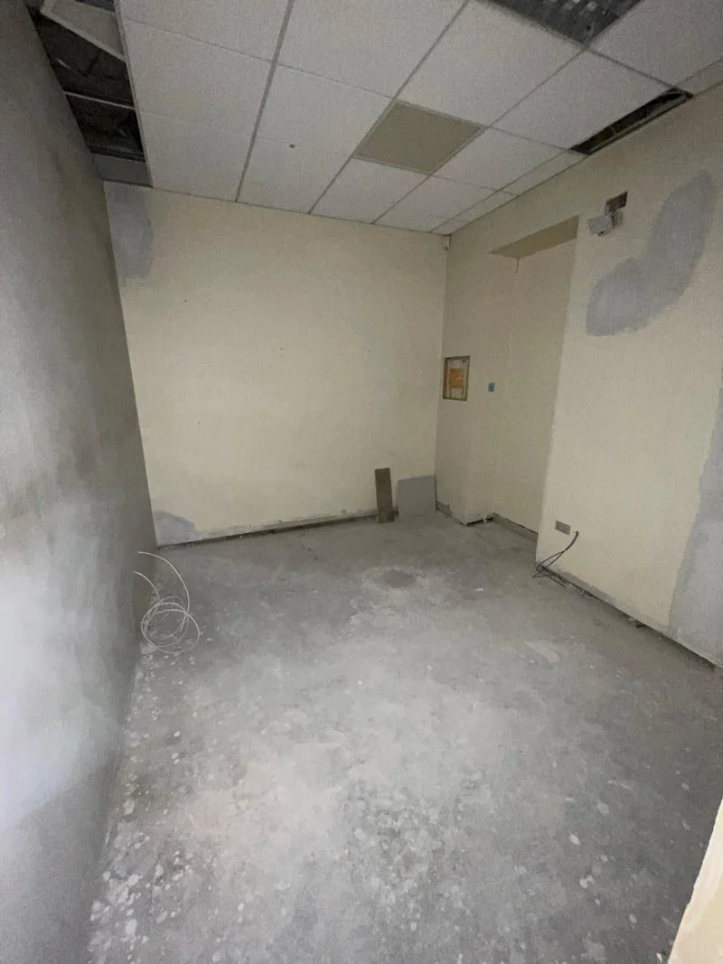 Empty room under renovation with unfinished walls, exposed wiring, and a drop ceiling with missing tiles.