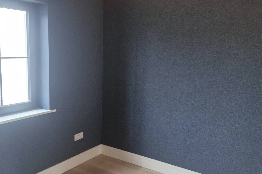 Empty room with light hardwood floor, blue textured walls, white window frame, and white baseboards.
