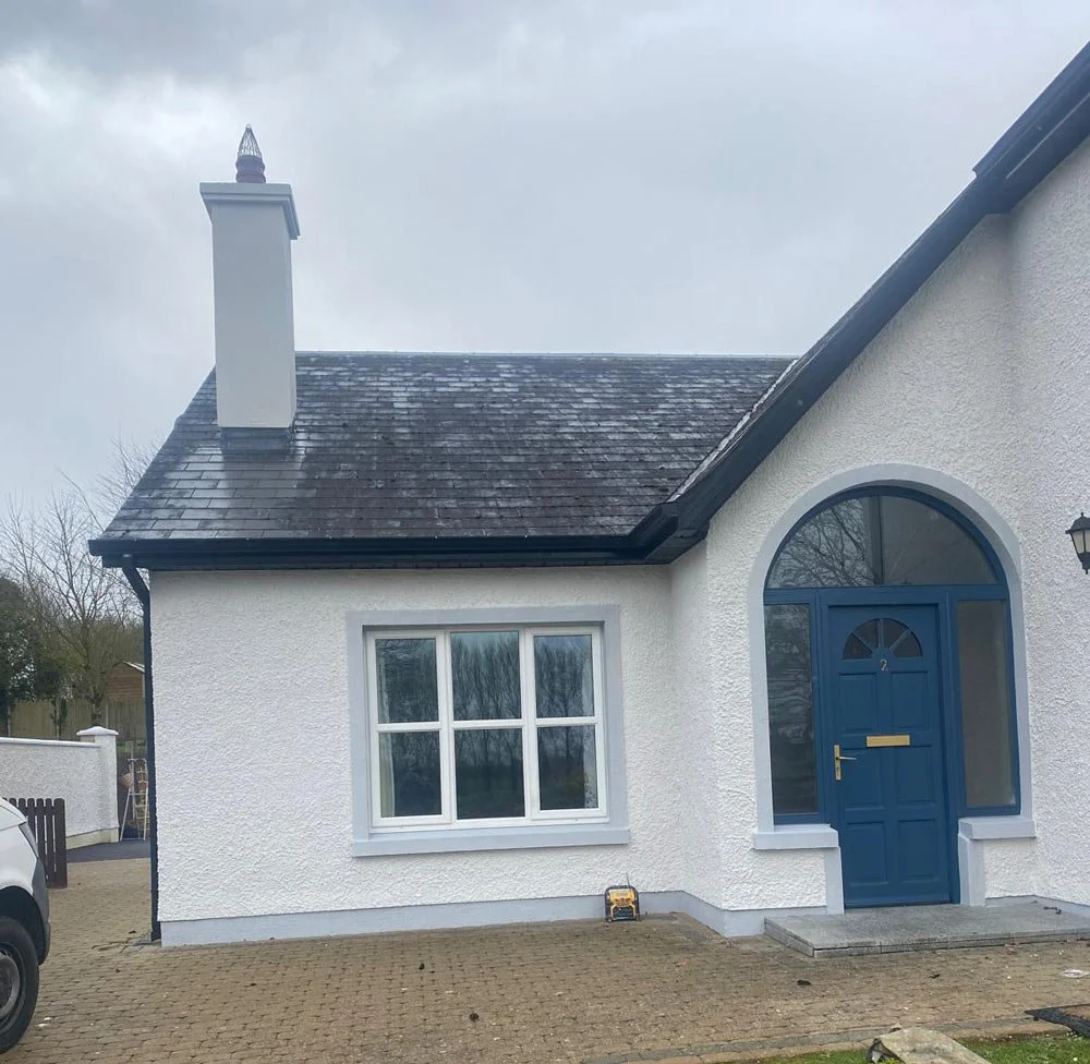 White house with blue door and arched window, paving stones in front, overcast sky.