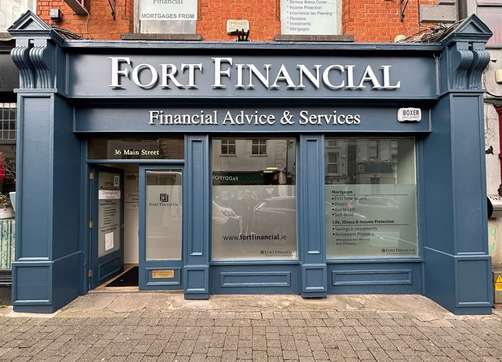 Storefront with blue facade and white lettering reading 'Fort Financial' and 'Financial Advice & Services,' located at 36 Main Street. Large windows on either side of a door displaying the website 'www.fortfinancial.ie' and list of services on the right window.