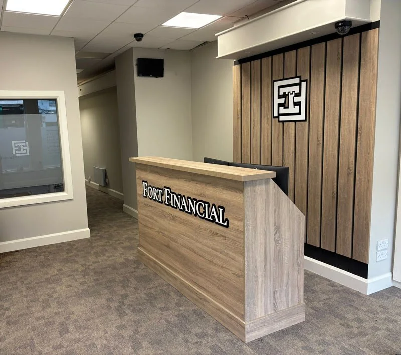 Reception desk with 'Fort Financial' sign in an office lobby, with a wooden panel wall and a logo on the wall behind the desk.