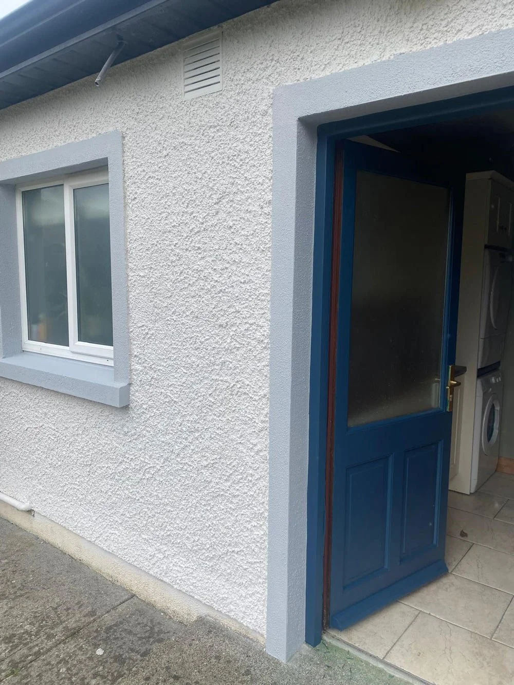 Exterior view of a house showing a window and an open door leading into a laundry room with a washing machine.
