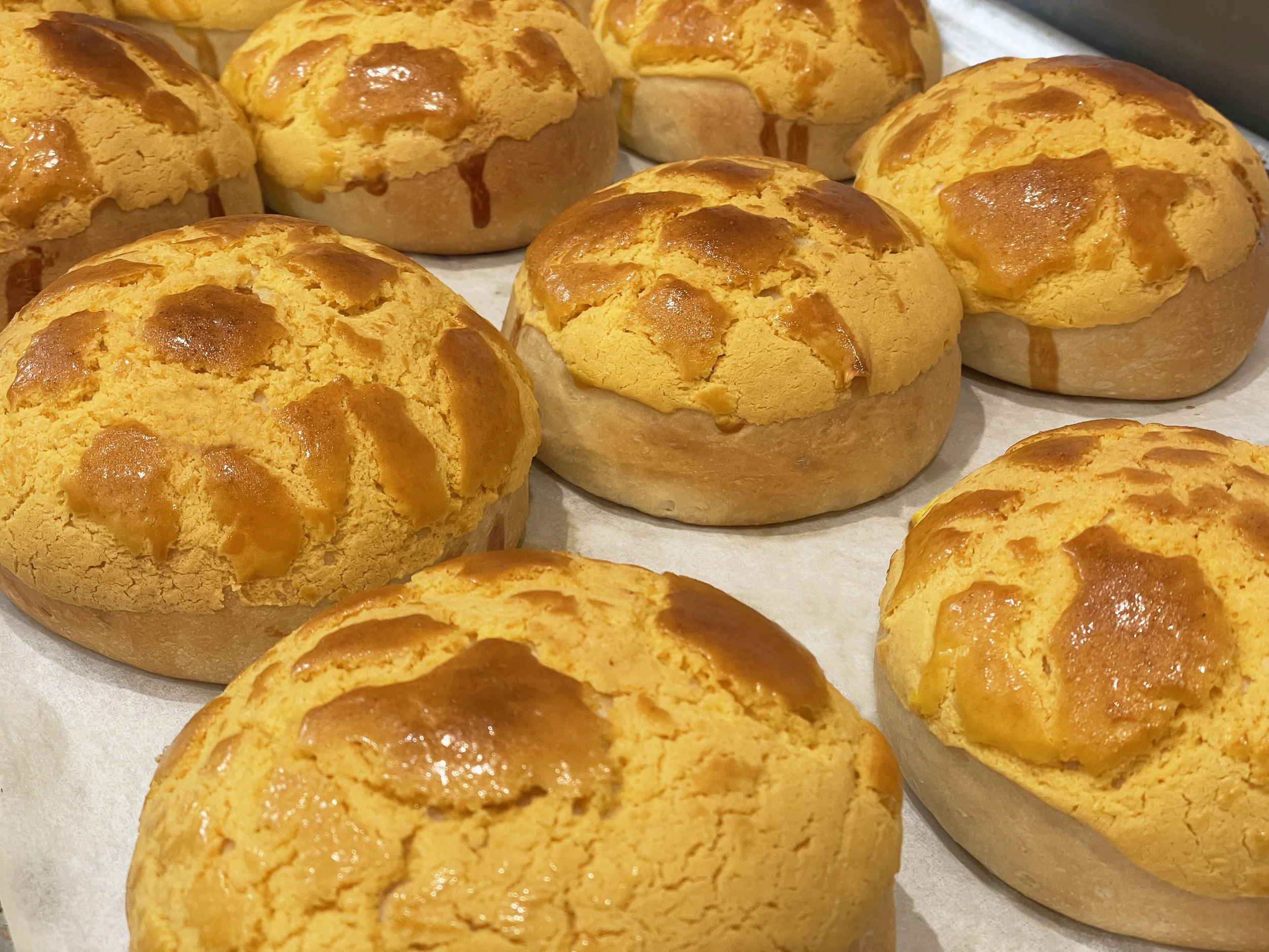 Golden-brown Brazilian cheese bread rolls on baking paper.