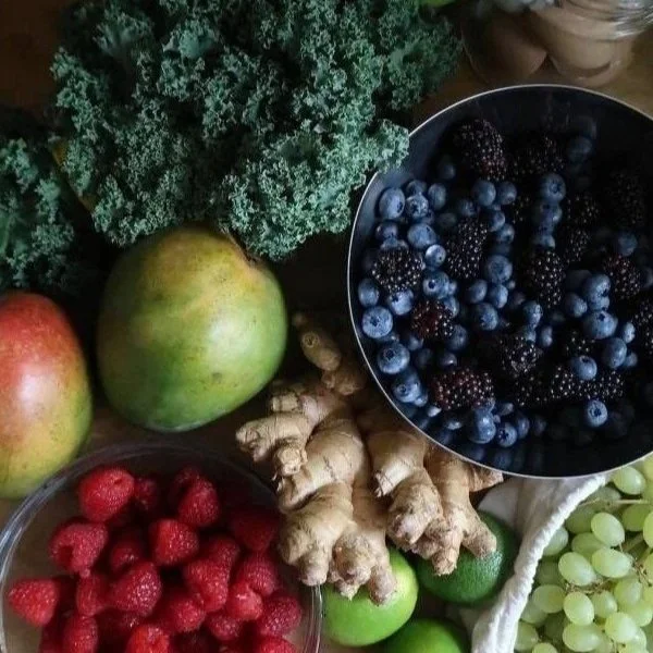 Fresh fruits and vegetables, including red raspberries, blackberries, blueberries, green grapes, apples, lime, ginger root, kale, and a light-colored vegetable.