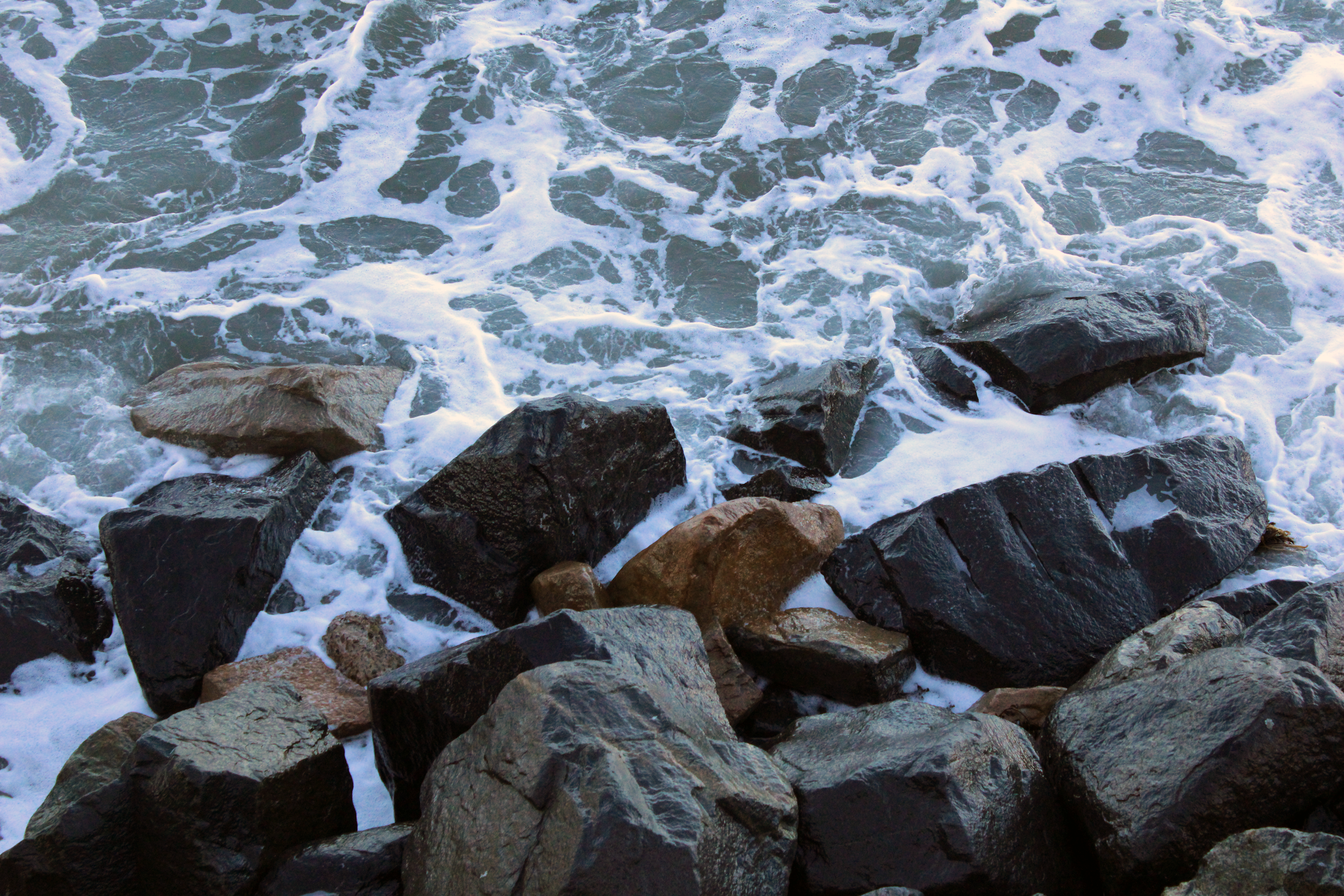 Rocks along a shoreline with waves crashing and white foam.