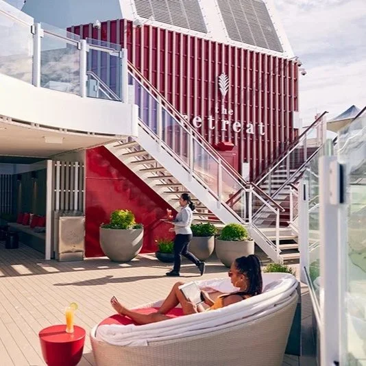 People relaxing outside a modern cruise ship with the word 'Retreat' on the building facade.