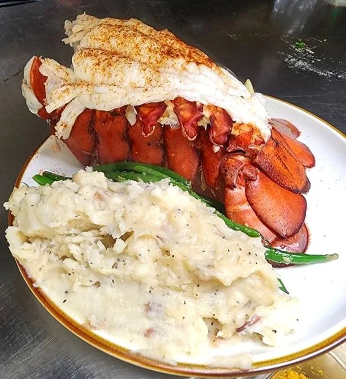 A plate of food with mashed potatoes, green beans, and a large  lobster.
